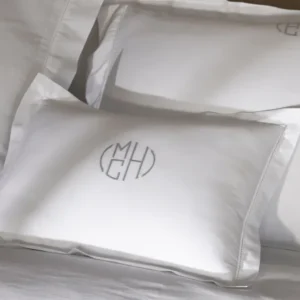 Close-up of white pillows featuring elegant monograms '(MCH)' and '(EH)' on soft cotton fabric, placed neatly on a bed. Featuring Bergamo Hemstitch bedding by Matouk. Available at Linen Society.