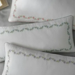 Matouk Daphne Matelassé white pillow shams with floral embroidered garland border.