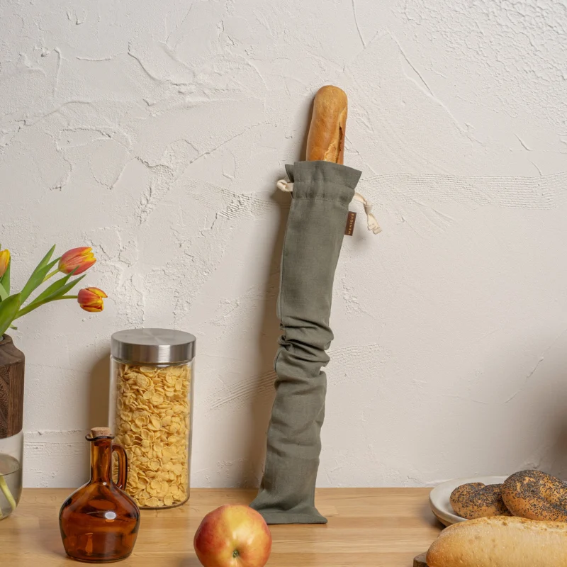 Long Bread bag hanging on a hook with bread and kitchen items on a table.