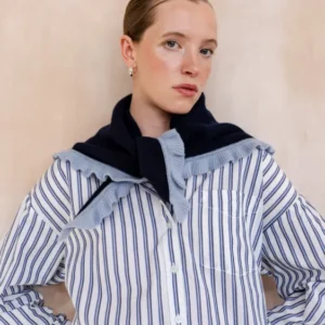 Woman models TBCo Merino Wool Triangle Scarf in Navy Ruffle, draped over shoulders, showcasing its light-blue ruffle trim and soft merino wool texture.