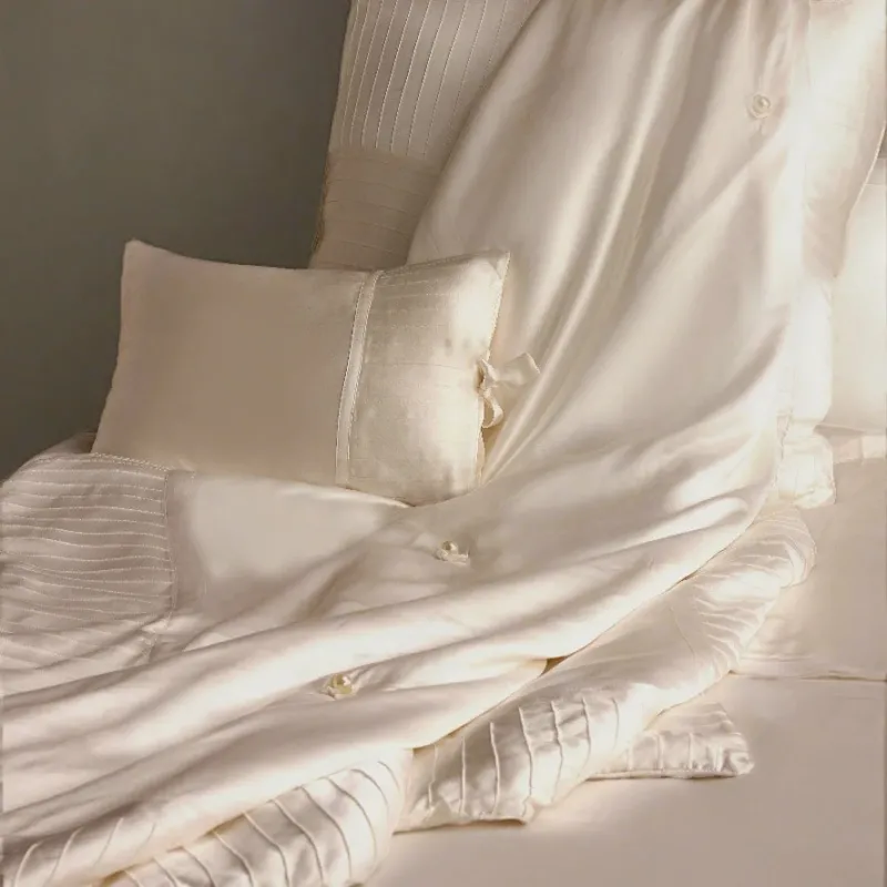 Kumi Kookoon ivory silk-filled throw with pleated texture draped over bed with matching pillow.